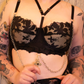 Person wearing black lace lingerie with chains against a textured wall.