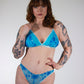 Woman wearing a blue lingerie set with tattoos on her arms and legs against a white background