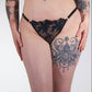 Person wearing black lace lingerie with tattoos on arms and legs against a white background