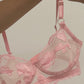 Pink lace bra held by a hand against a beige background