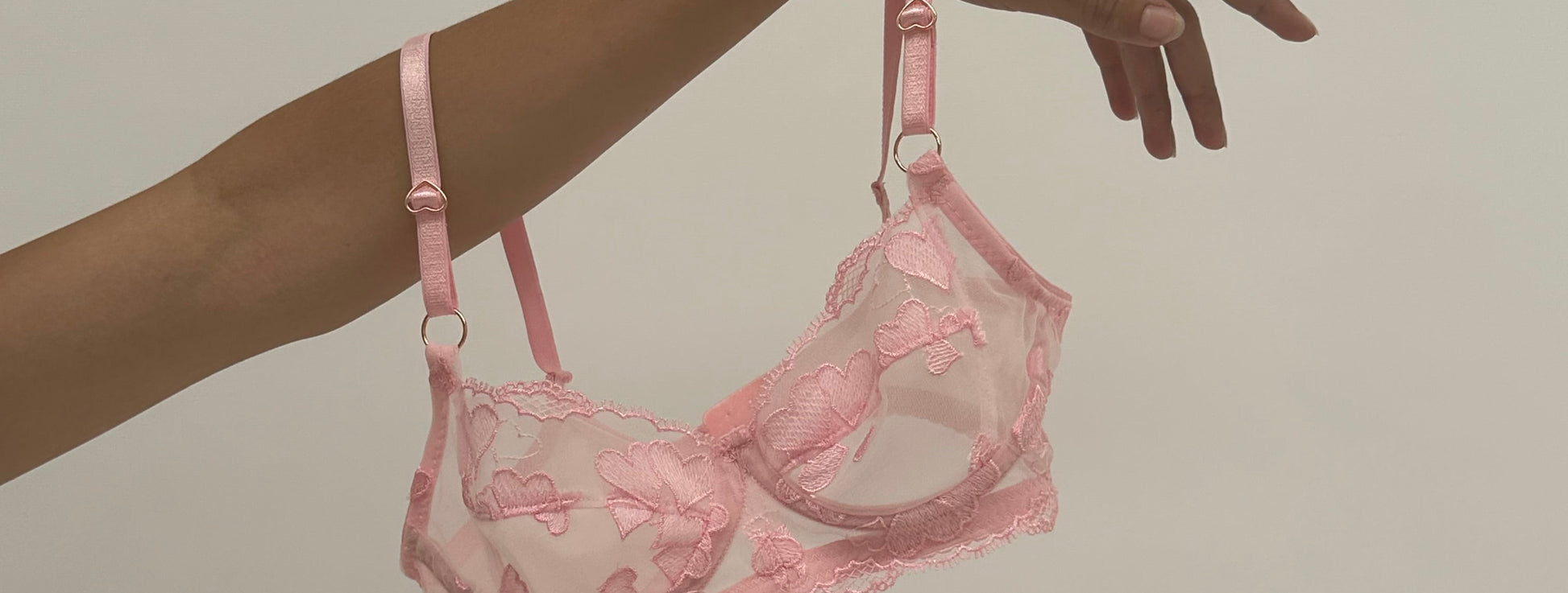 Pink lace bra held by a hand against a beige background