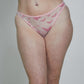A woman modeling a light pink sheer mesh lingerie set with a darker pink abstract pattern, consisting of a triangle bra and matching thong, paired with white socks against a plain light gray studio background.