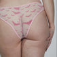 A woman shown from the back wearing a light pink lingerie set with a subtle pattern, standing against a plain light gray studio background.