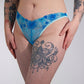Person wearing blue lace underwear with tattoos on arms and legs against a white background