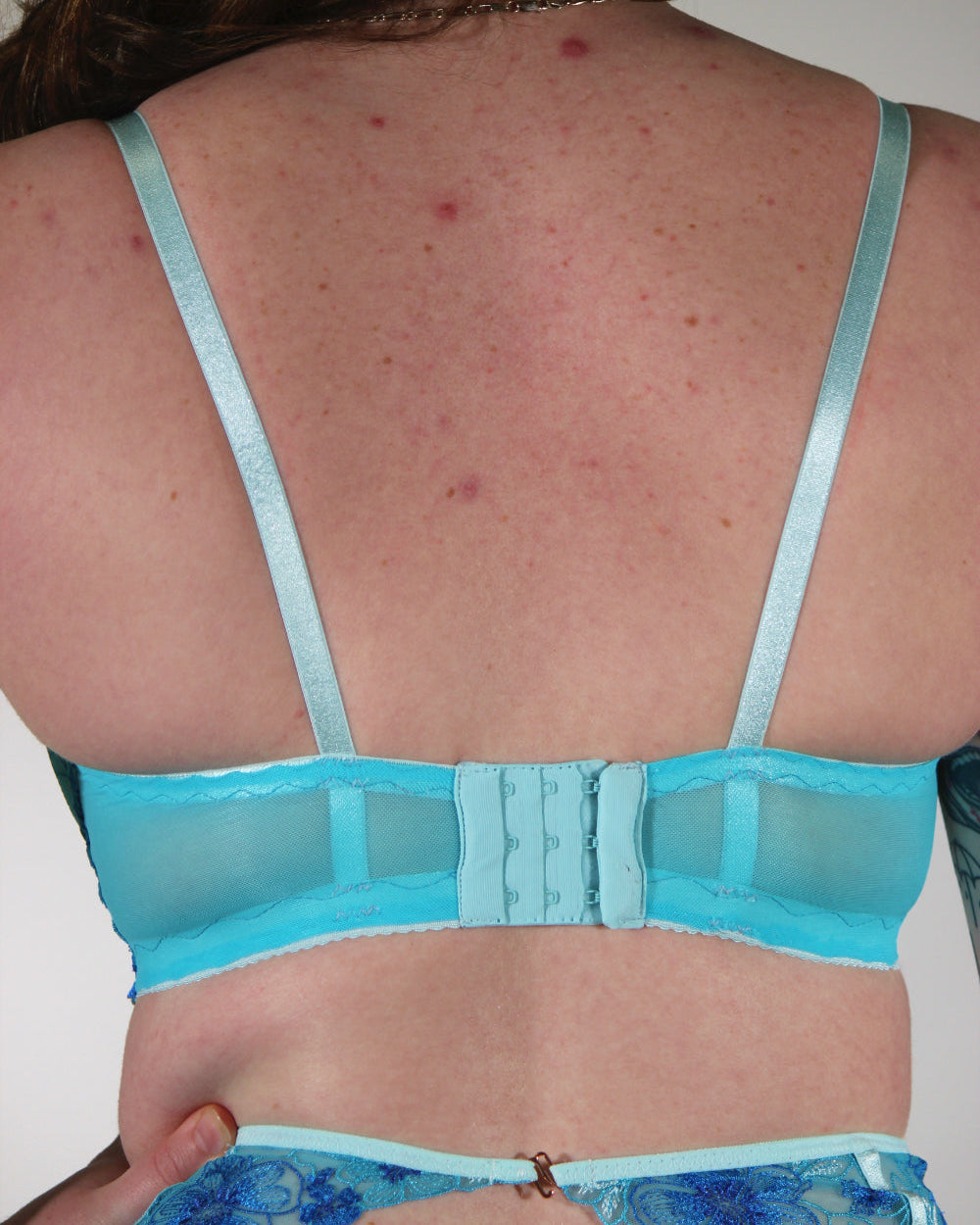 Person wearing a blue bra and underwear set with a plain background