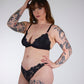 Woman wearing black lingerie with tattoos on arms and legs against a white background