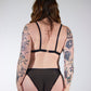 Person wearing a black strappy outfit with floral tattoos on arms and back against a white background
