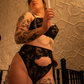 Person in black lingerie holding a lit candle against a textured wall.