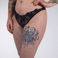 Person wearing black lace lingerie with tattoos on arms and legs against a white background